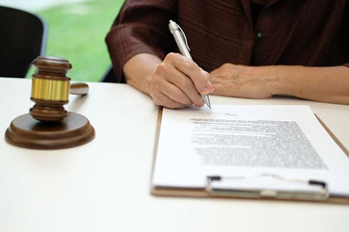 person writing on a contract next to a gavel